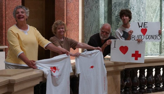 four people holding signs/shirts about donating blood