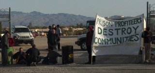 People blocking the entrance with sign saying "prison profiteers destroy communities."
