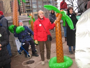 Rally participants carry inflated palm trees, mocking footage from Fox News of a "Wisconsin" rally highlighting angry pro-union protesters with palm trees in the background